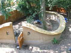 an outdoor play area in the middle of some trees and dirt with stairs leading up to it