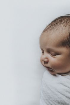 a baby wrapped in a white blanket sleeping on top of it's back with its eyes closed