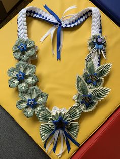 an origami necklace made out of dollar bills on a yellow tablecloth with blue ribbons