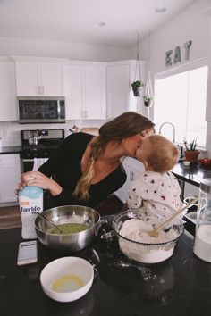 a woman holding a baby in her arms while mixing food on the kitchen counter top