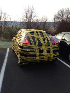 two cars parked in a parking lot with yellow tape wrapped around the car's sides