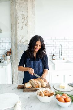 a woman in an apron slicing bread on a cutting board with a knife and fork