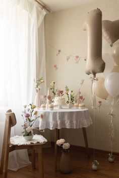 a table topped with cupcakes and balloons next to a white table cloth covered table