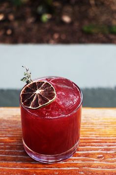 a red drink sitting on top of a wooden table next to a slice of orange