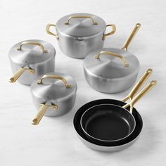 four pots and three pans with gold handles on a white countertop next to each other