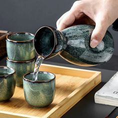 a person pouring water into four green cups