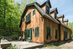 a wooden house with green shutters on the front and side windows, surrounded by trees