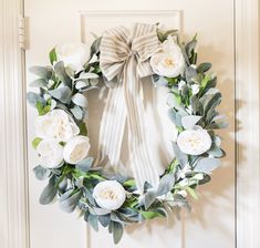 a wreath with white flowers and greenery hangs on a door