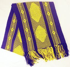 a purple and yellow scarf with fringes on white table top next to black wall