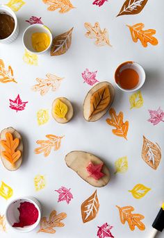 several different types of autumn leaves on a white tablecloth with paint and paper cups