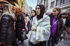 several women are walking down the street in front of some buildings and one woman is wearing a scarf