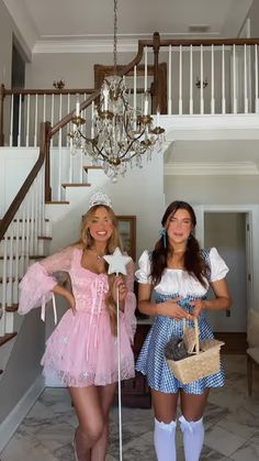 two women dressed in costume standing next to each other near stairs and chandelier