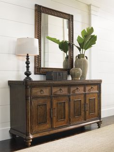 a large mirror sitting on top of a wooden dresser next to a lamp and vase