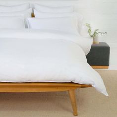 a bed with white sheets and pillows on top of it in a room next to a plant