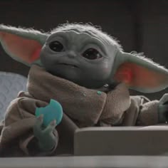 the child yoda is sitting at a desk and holding a toy in his hand