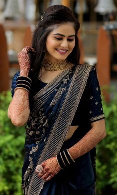 a woman wearing a blue sari and holding her hands up to her face, smiling