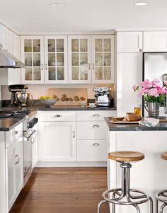 a kitchen with white cabinets and counter tops has stools in front of the island