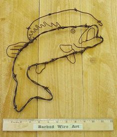 a wooden floor with a ruler and wire sculpture on it's side that says, barbwire art