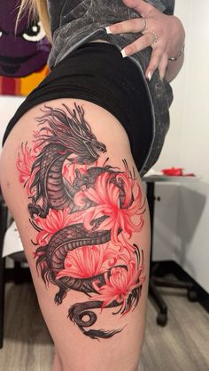 a woman's thigh with a dragon tattoo on her leg and red flowers in the background