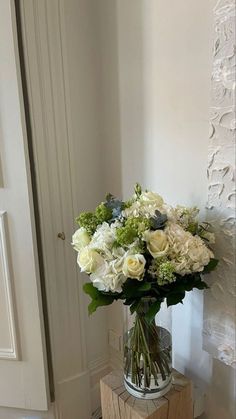 a vase filled with white flowers sitting on top of a wooden table next to a door