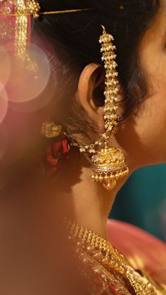 a close up of a woman's face with gold jewelry on her neck and ear