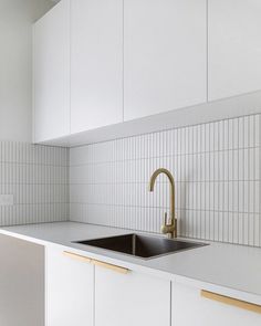 a kitchen with white cabinets and gold faucet