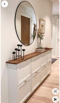 a mirror is hanging on the wall above a white cabinet with drawers and hooks in front of it