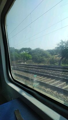 the view from inside a train window looking at railroad tracks and trees in the distance