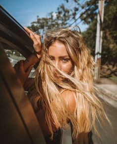 a woman with long blonde hair leaning out the window of a car looking into the camera