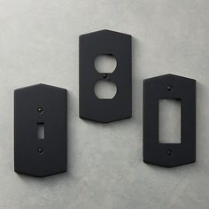 three black switchplates are shown on a gray surface with holes in the middle