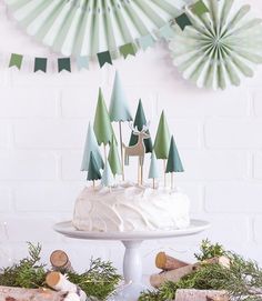 a white cake with green trees on top and a deer decoration hanging from the ceiling