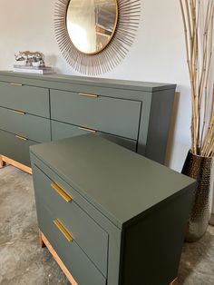 two green dressers with gold handles in front of a mirror and vase on the wall