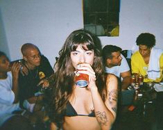 a woman drinking from a can while sitting at a table with other people in the background