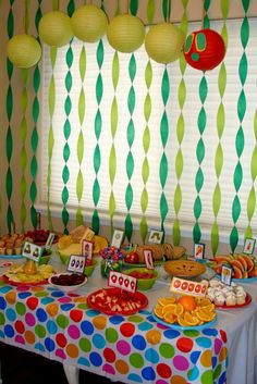 a table topped with lots of food next to a window covered in green and white curtains