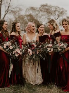 a group of women standing next to each other wearing red dresses and holding bouquets