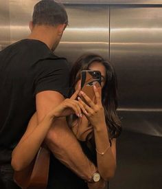 a man and woman standing in front of an elevator taking pictures with their cell phones