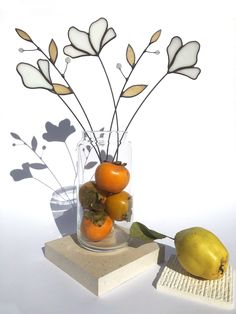 a vase filled with flowers and fruit sitting on top of a wooden block next to a book