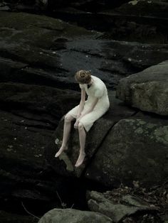 a woman sitting on top of a large rock