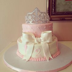 a pink and white cake with a tiara on top, sitting on a table