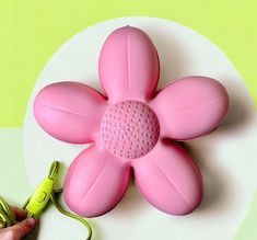 a pink flower shaped object being held by a person's hand with a green cord