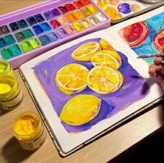 a person is painting some lemons on a book with watercolors in front of them