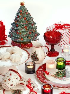 a table topped with plates and candles next to a christmas tree on top of a table