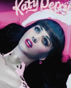 a woman with black hair and blue eyes posing in front of a pink sign that says kitty perk