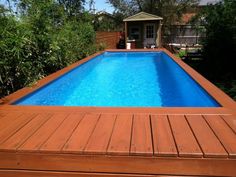 a wooden deck next to a swimming pool in a yard with trees and bushes around it