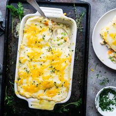 a casserole dish with chicken and cheese in it on a baking tray next to two plates