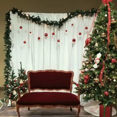 a red couch sitting next to a christmas tree in front of a white drapes