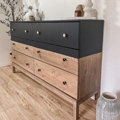 a black and brown dresser sitting on top of a wooden floor next to a vase