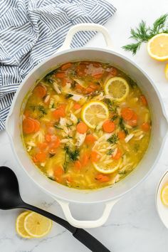 a white pot filled with soup next to sliced lemons and carrots on a table