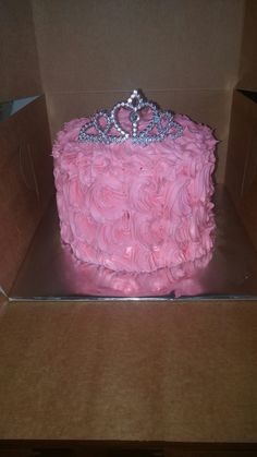 a pink cake in a box with a tiara on top