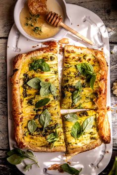 a white plate topped with a cheesy quiche next to a bowl of sauce